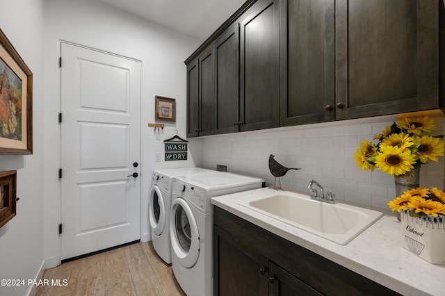 laundry area with washing machine and clothes dryer, sink, cabinets, and light wood-type flooring