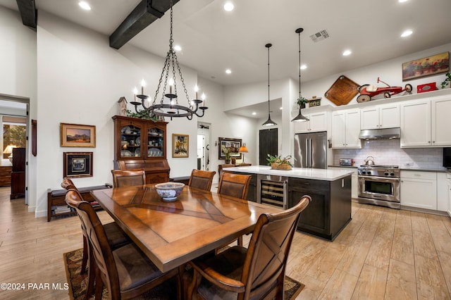 dining space with beverage cooler, a towering ceiling, a chandelier, and light wood-type flooring