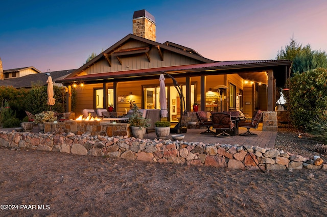 back house at dusk featuring a patio and an outdoor living space with a fire pit