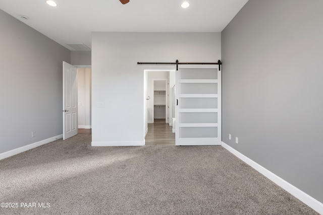 unfurnished bedroom featuring ceiling fan, carpet, a barn door, and a spacious closet