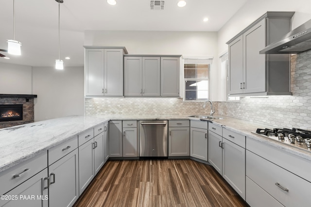 kitchen with appliances with stainless steel finishes, decorative light fixtures, wall chimney range hood, sink, and gray cabinets