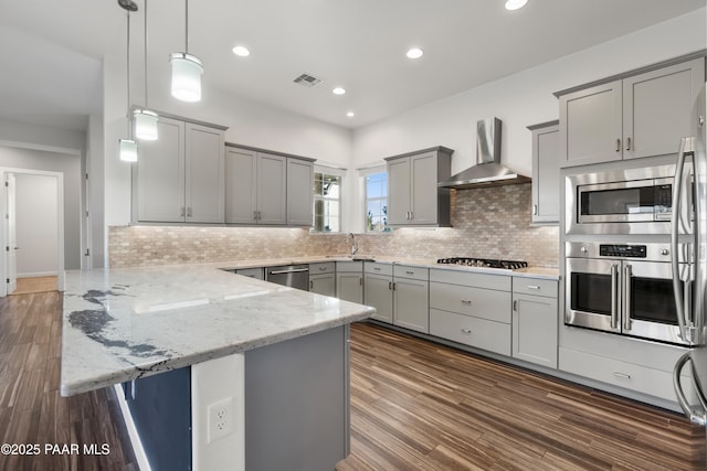 kitchen with a kitchen bar, wall chimney range hood, stainless steel appliances, hanging light fixtures, and kitchen peninsula