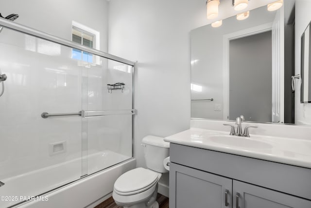 full bathroom with enclosed tub / shower combo, vanity, and toilet