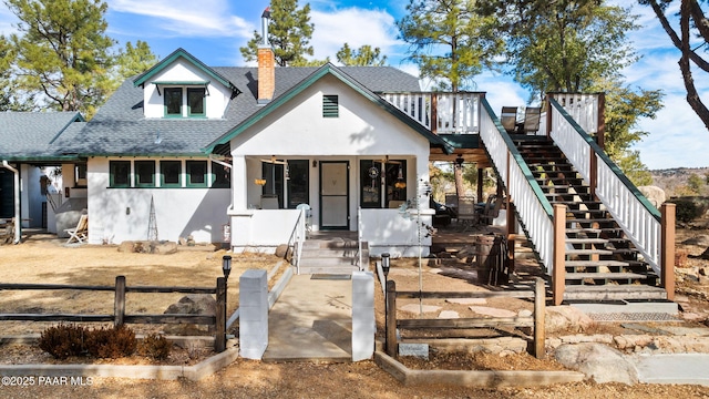 view of front facade featuring roof with shingles, a chimney, stucco siding, stairway, and fence