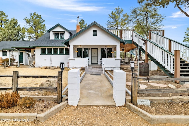 view of front of property featuring stairs, roof with shingles, a chimney, and stucco siding