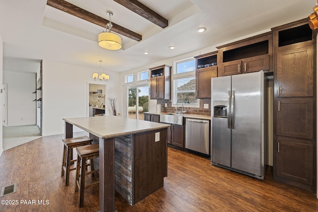 kitchen featuring open shelves, a sink, beamed ceiling, appliances with stainless steel finishes, and a notable chandelier