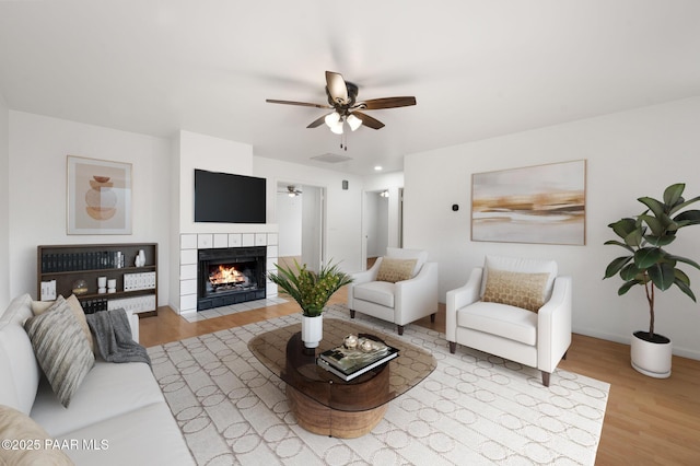 living room featuring a tile fireplace, ceiling fan, and light hardwood / wood-style flooring