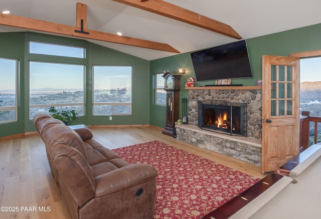 living room with vaulted ceiling with beams, a stone fireplace, light hardwood / wood-style flooring, and a healthy amount of sunlight