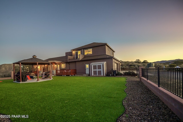 back house at dusk with a yard, a gazebo, a mountain view, and a storage unit