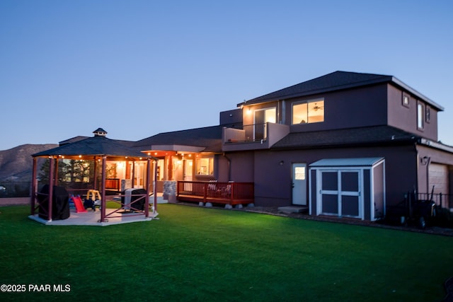 back house at dusk featuring a gazebo, a balcony, a yard, a deck with mountain view, and a patio