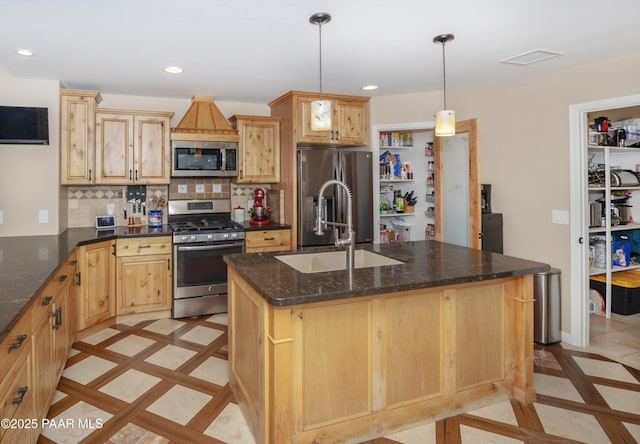 kitchen with stainless steel appliances, an island with sink, hanging light fixtures, and dark stone counters