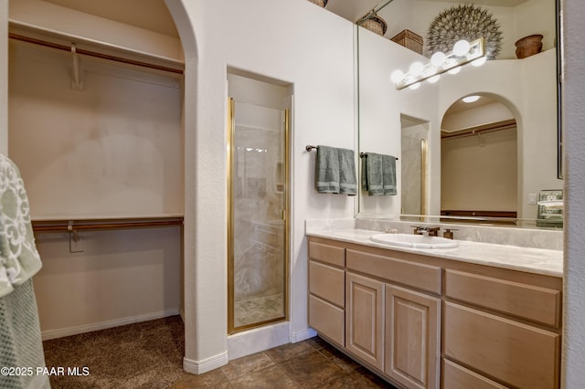 full bathroom with a walk in closet, vanity, a stall shower, and baseboards