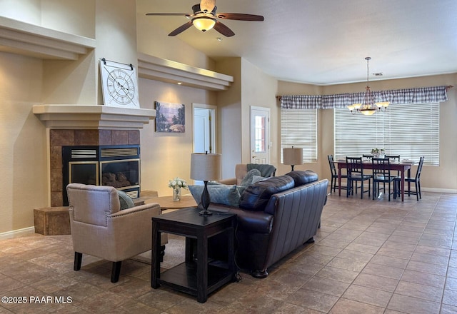 living room with ceiling fan with notable chandelier, a tile fireplace, a high ceiling, and baseboards