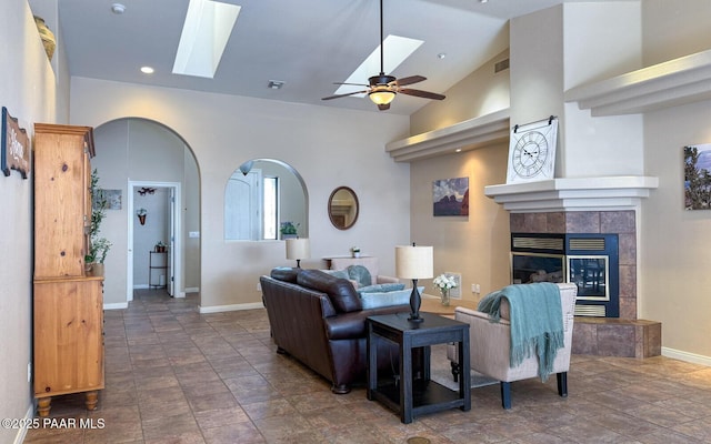 living room with visible vents, a tile fireplace, a skylight, arched walkways, and high vaulted ceiling