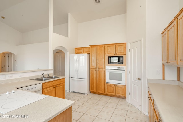 kitchen featuring light brown cabinetry, white appliances, sink, light tile patterned floors, and high vaulted ceiling