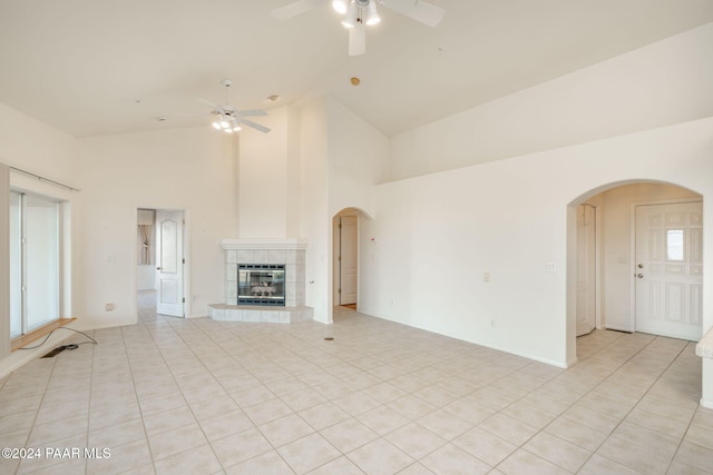 unfurnished living room featuring ceiling fan, light tile patterned floors, a tile fireplace, and high vaulted ceiling