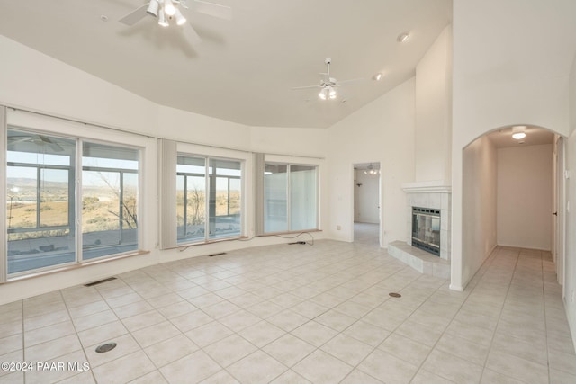 unfurnished living room featuring ceiling fan, light tile patterned floors, a fireplace, and high vaulted ceiling