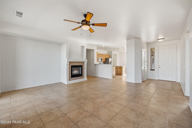 unfurnished living room featuring light tile patterned flooring, ceiling fan, and a tiled fireplace