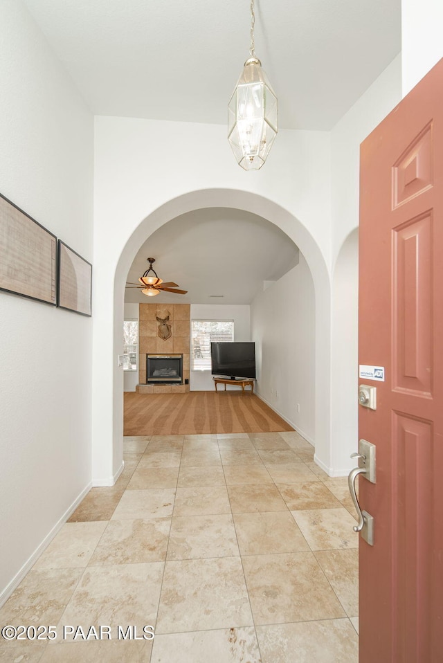 corridor featuring baseboards, arched walkways, and light tile patterned flooring