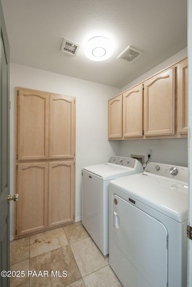 clothes washing area featuring visible vents, cabinet space, a textured ceiling, and separate washer and dryer