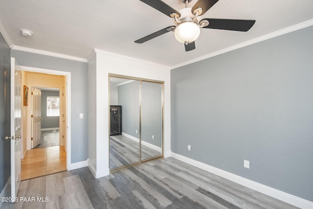 unfurnished bedroom featuring a ceiling fan, wood finished floors, baseboards, ornamental molding, and a closet