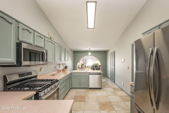 kitchen with green cabinetry, a peninsula, vaulted ceiling, light countertops, and appliances with stainless steel finishes