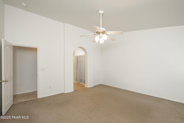 carpeted empty room featuring arched walkways, baseboards, ceiling fan, and a towering ceiling