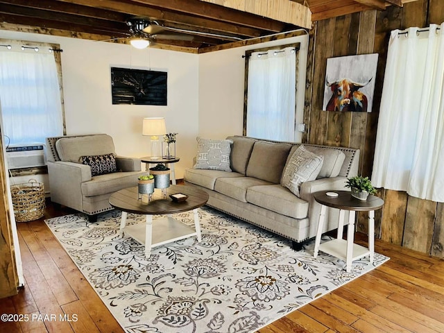 living area with beamed ceiling, wood walls, hardwood / wood-style floors, and ceiling fan