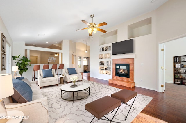 living room featuring built in shelves, ceiling fan, hardwood / wood-style floors, and a tile fireplace