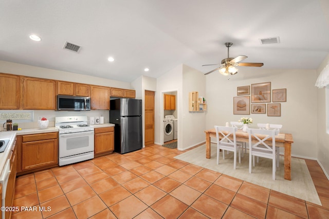 kitchen featuring vaulted ceiling, white range with gas stovetop, washing machine and clothes dryer, light tile patterned floors, and black fridge