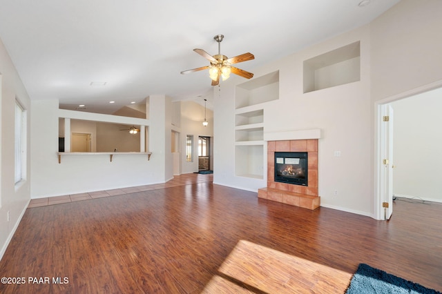 unfurnished living room featuring dark hardwood / wood-style floors, high vaulted ceiling, a fireplace, ceiling fan, and built in shelves