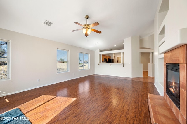 unfurnished living room with a tiled fireplace, dark wood-type flooring, high vaulted ceiling, and ceiling fan