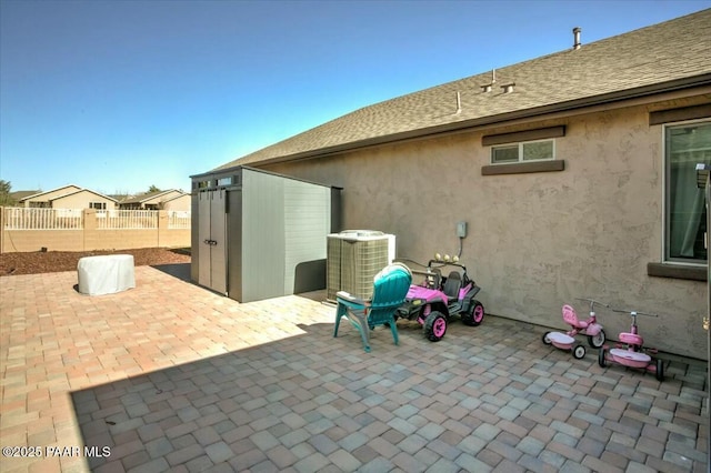 view of patio featuring an outbuilding, central AC unit, a storage unit, and fence