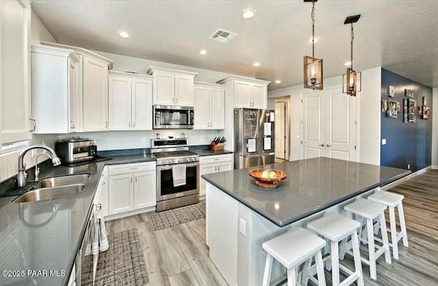 kitchen featuring dark countertops, visible vents, stainless steel appliances, white cabinetry, and a sink