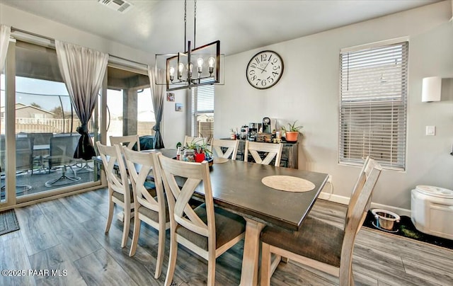 dining area with a notable chandelier, visible vents, baseboards, and wood finished floors