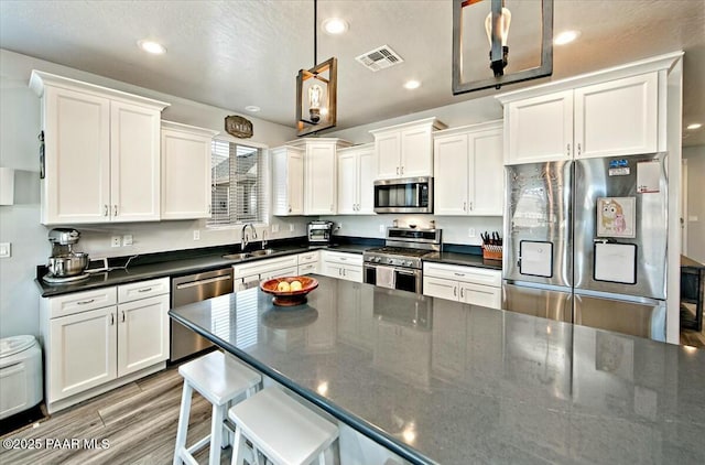 kitchen with dark countertops, visible vents, appliances with stainless steel finishes, white cabinetry, and a sink