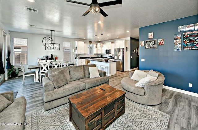 living area with visible vents, ceiling fan with notable chandelier, recessed lighting, light wood finished floors, and baseboards