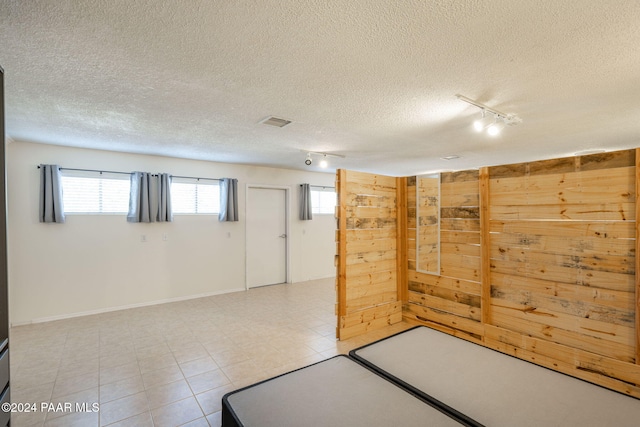 basement with a textured ceiling, rail lighting, and wooden walls