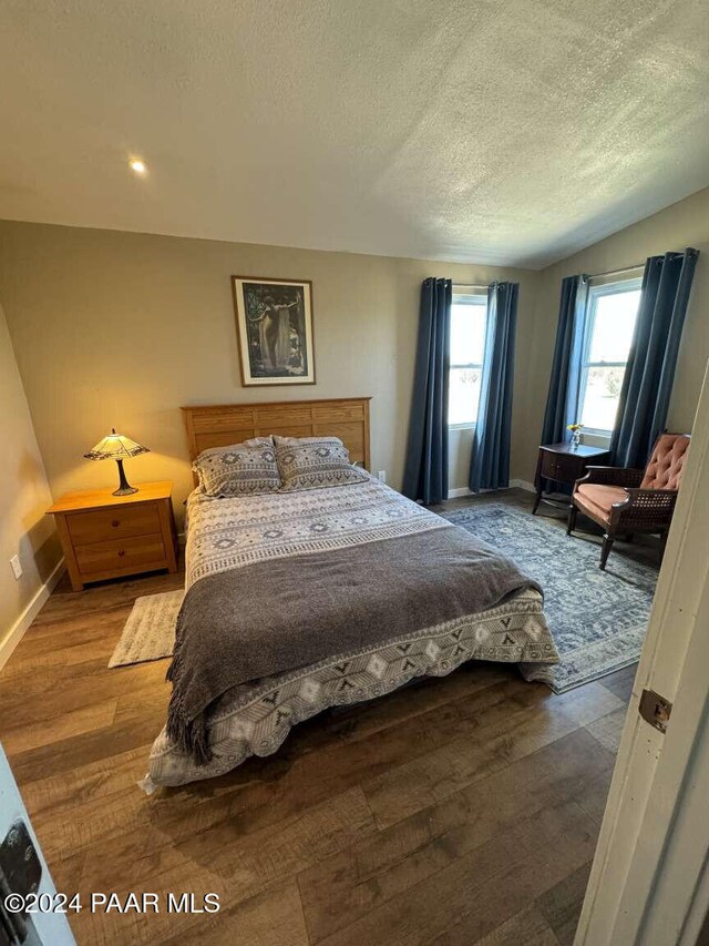 bedroom featuring vaulted ceiling, a textured ceiling, and hardwood / wood-style flooring