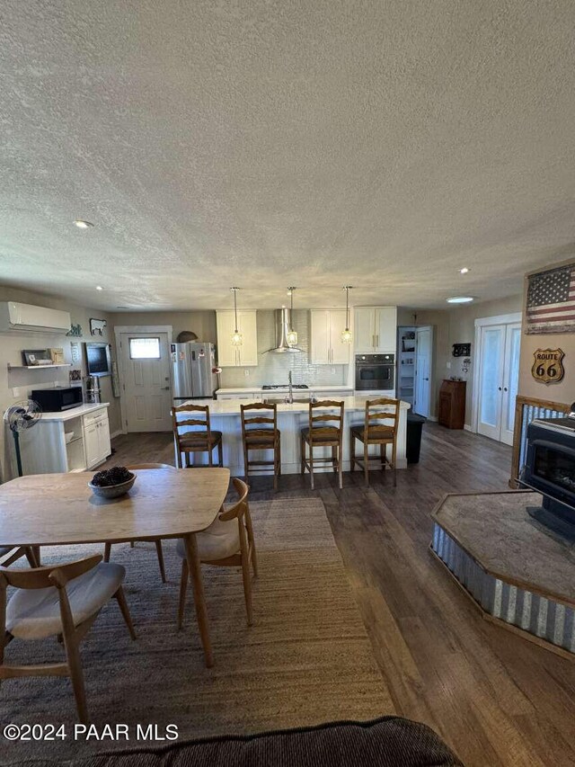 dining area featuring a wood stove, a textured ceiling, an AC wall unit, and dark wood-type flooring