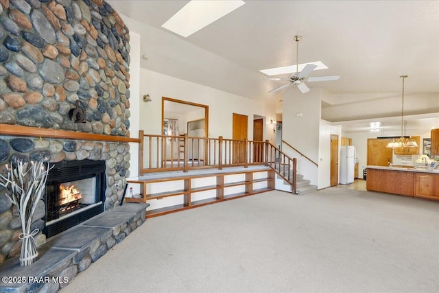 carpeted living room with a stone fireplace, high vaulted ceiling, ceiling fan, and a skylight