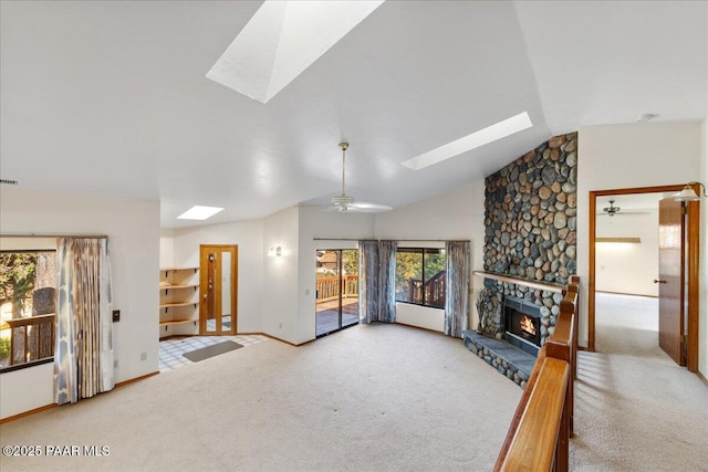 carpeted living room with ceiling fan, a stone fireplace, and vaulted ceiling with skylight