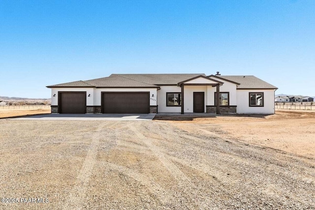 view of front of house with stone siding, a garage, dirt driveway, and stucco siding