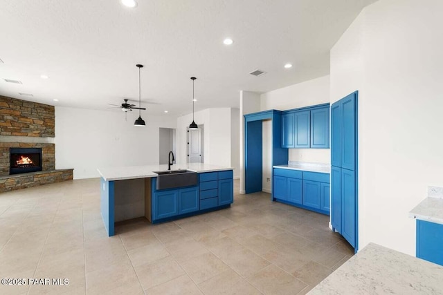 kitchen featuring visible vents, open floor plan, a stone fireplace, a ceiling fan, and a sink