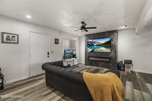 living room with ceiling fan, a stone fireplace, wood-type flooring, and a textured ceiling