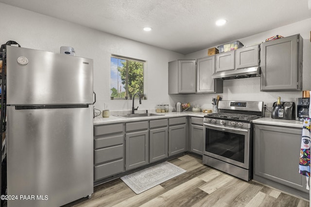 kitchen with appliances with stainless steel finishes, light hardwood / wood-style floors, a textured ceiling, sink, and gray cabinets