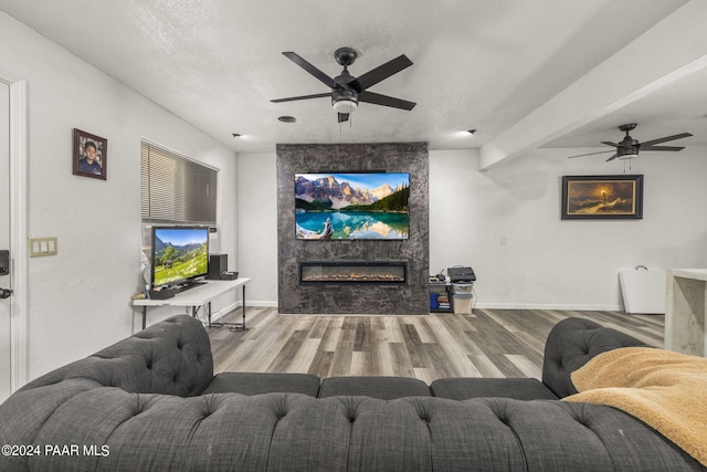 living room featuring hardwood / wood-style floors, a textured ceiling, a stone fireplace, and ceiling fan