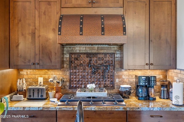 965 Northwood Loop, Prescott, AZ 86303 - kitchen featuring range hood, stainless steel gas stovetop, tasteful backsplash, brown cabinets, and light stone counters