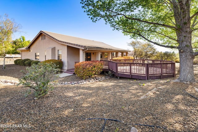 rear view of house with a deck, a tile roof, and stucco siding