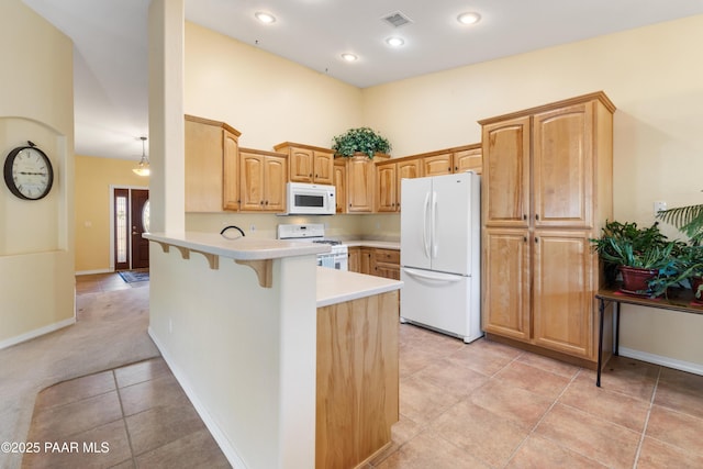 kitchen featuring white appliances, a kitchen breakfast bar, light countertops, a peninsula, and visible vents